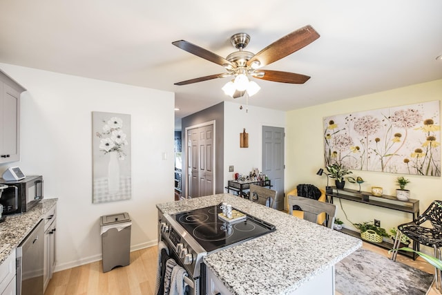 kitchen featuring baseboards, light wood-style flooring, a kitchen island, light stone counters, and stainless steel appliances