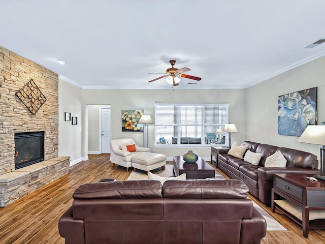 living room with ornamental molding, visible vents, a stone fireplace, and wood finished floors