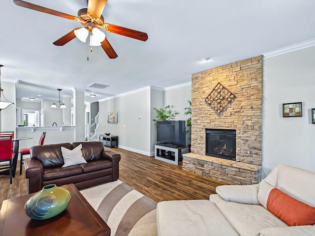 living room with ornamental molding, visible vents, a stone fireplace, and wood finished floors