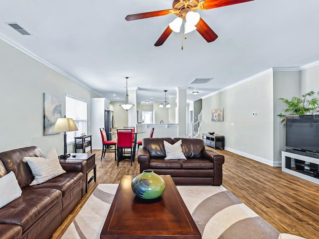 living area with baseboards, visible vents, ceiling fan, ornamental molding, and light wood-style floors