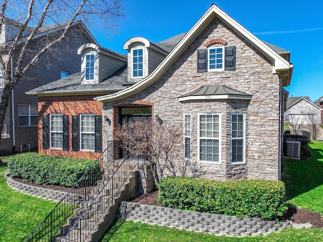 view of front of property featuring brick siding, cooling unit, and a front yard