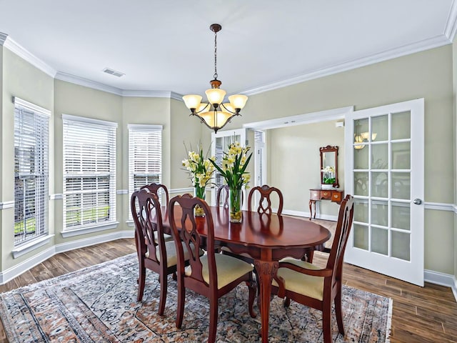 dining space featuring visible vents, baseboards, wood finished floors, an inviting chandelier, and crown molding