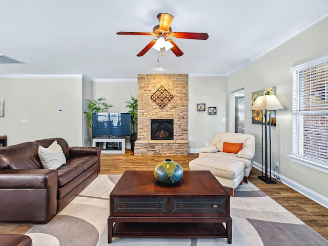 living room with baseboards, visible vents, wood finished floors, crown molding, and a stone fireplace