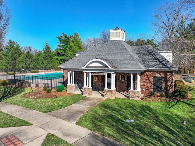 exterior space with a shingled roof, a community pool, fence, and brick siding