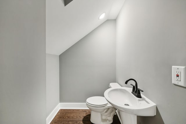 half bath with baseboards, toilet, wood finished floors, vaulted ceiling, and a sink