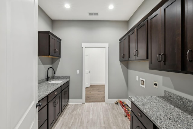 kitchen with baseboards, visible vents, light stone counters, dark brown cabinets, and a sink