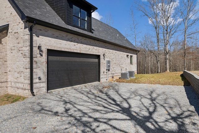 view of side of property with a shingled roof, central AC unit, aphalt driveway, and brick siding