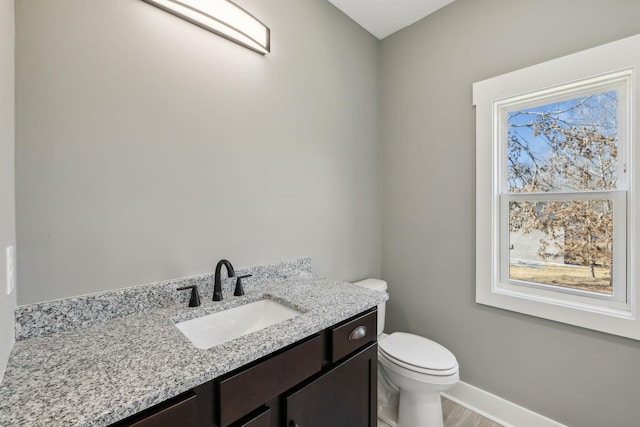 half bathroom featuring toilet, baseboards, and vanity