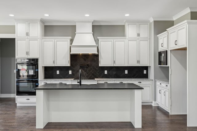 kitchen with dark wood finished floors, ornamental molding, an island with sink, premium range hood, and black appliances