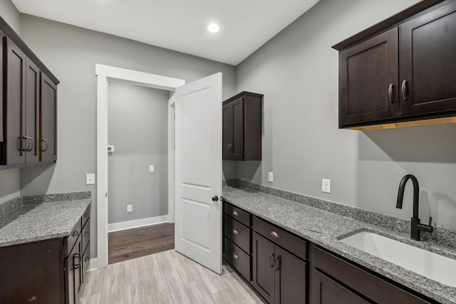 kitchen with baseboards, light stone counters, dark brown cabinets, light wood-type flooring, and a sink