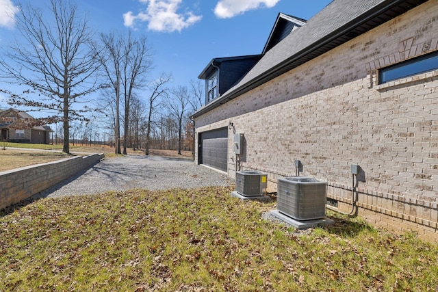 view of side of property featuring central AC, brick siding, and driveway