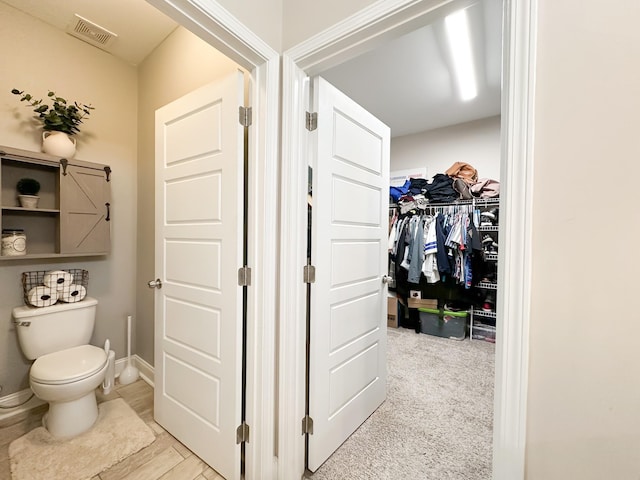 bathroom with a walk in closet, baseboards, visible vents, and toilet