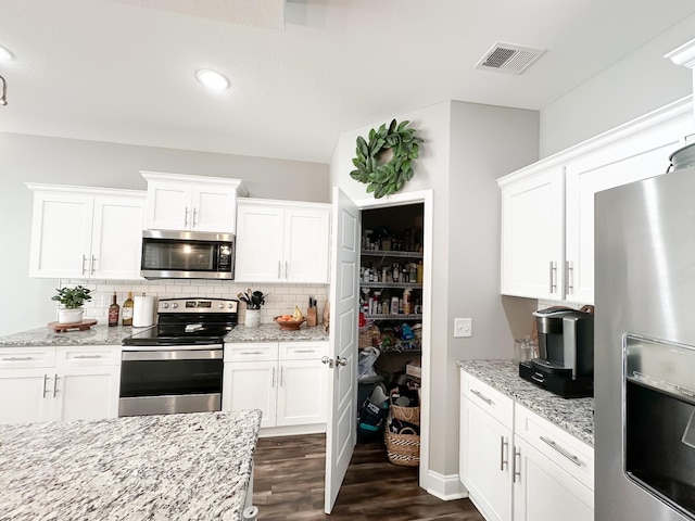 kitchen with dark wood-style flooring, stainless steel appliances, tasteful backsplash, visible vents, and white cabinets