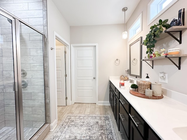 bathroom featuring wood finish floors, double vanity, a sink, a shower stall, and baseboards