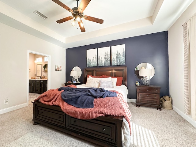 carpeted bedroom featuring ensuite bathroom, ceiling fan, visible vents, baseboards, and a tray ceiling