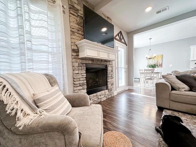 living room with baseboards, visible vents, dark wood-style flooring, an inviting chandelier, and a stone fireplace