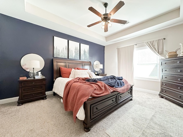 bedroom with light carpet, baseboards, a tray ceiling, and a ceiling fan