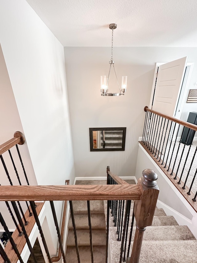 staircase featuring an inviting chandelier, baseboards, a textured ceiling, and carpet flooring