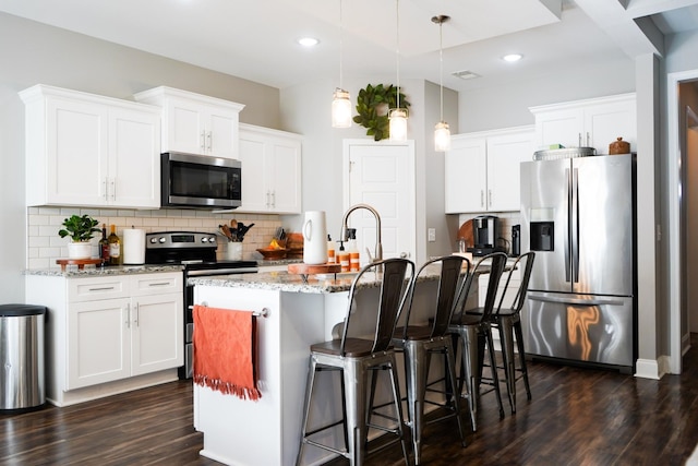 kitchen with an island with sink, appliances with stainless steel finishes, dark wood-type flooring, pendant lighting, and backsplash