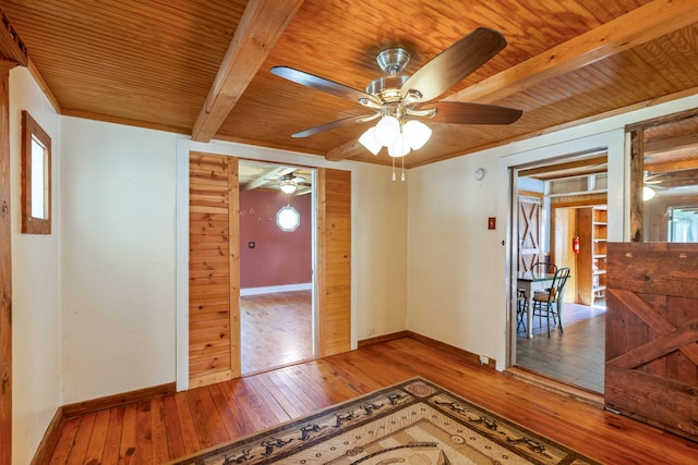 unfurnished room featuring wood-type flooring, ceiling fan, wooden ceiling, beamed ceiling, and baseboards