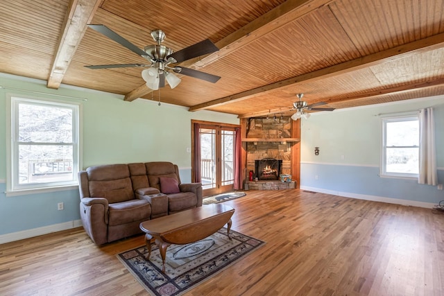 living area featuring beam ceiling, wooden ceiling, a stone fireplace, and wood finished floors