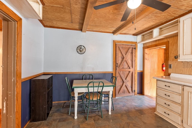 dining room featuring wooden ceiling, a wainscoted wall, beamed ceiling, and stone finish flooring