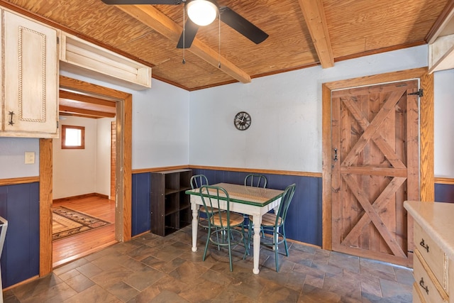 dining area with stone finish floor, wooden ceiling, a wainscoted wall, and beamed ceiling