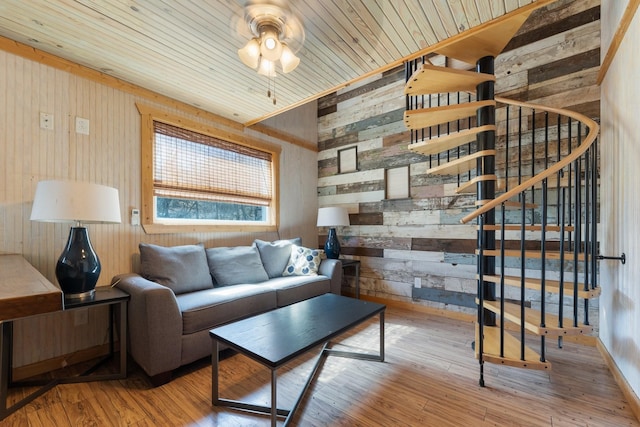 living room with wood walls, stairway, wood finished floors, and a ceiling fan