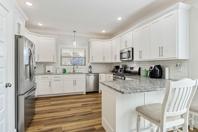 kitchen featuring dark wood finished floors, appliances with stainless steel finishes, white cabinets, a sink, and a peninsula