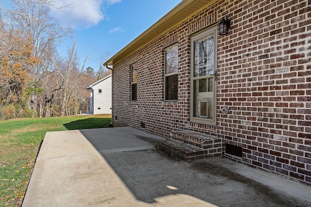 view of side of property with a lawn, a patio, and brick siding