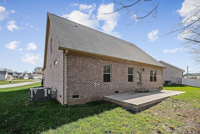 rear view of house with a shingled roof, a patio area, brick siding, and a lawn