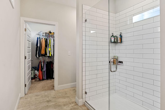 full bath featuring a spacious closet, a stall shower, and baseboards