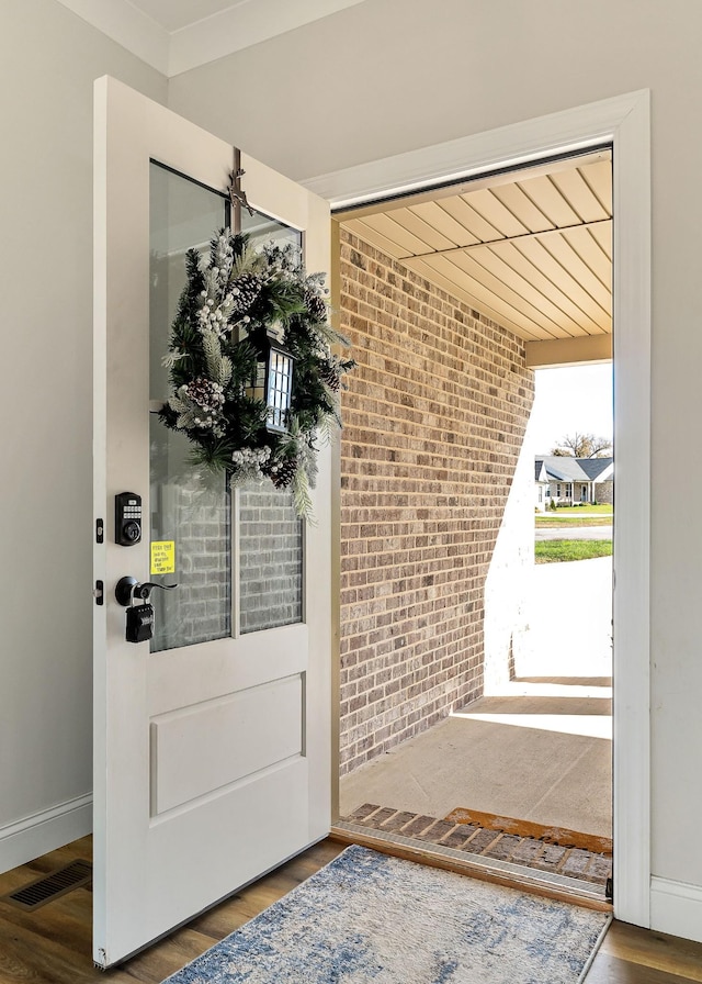 doorway featuring baseboards, visible vents, brick wall, and wood finished floors