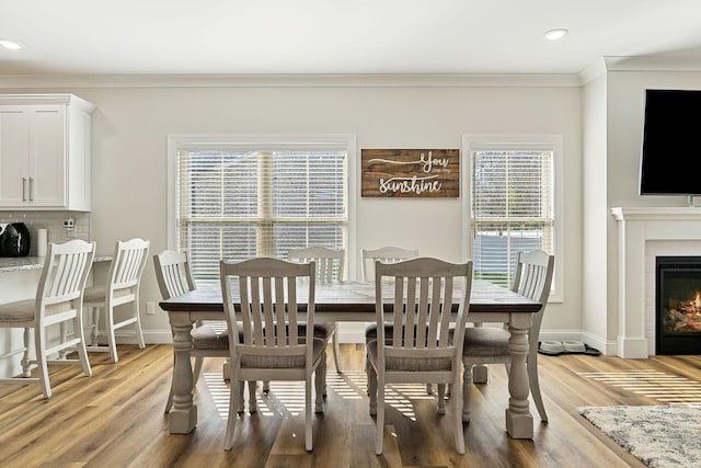 dining room featuring ornamental molding, light wood-type flooring, a glass covered fireplace, and baseboards