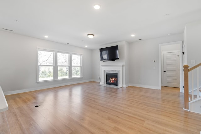 unfurnished living room with light wood finished floors, a premium fireplace, visible vents, and stairway