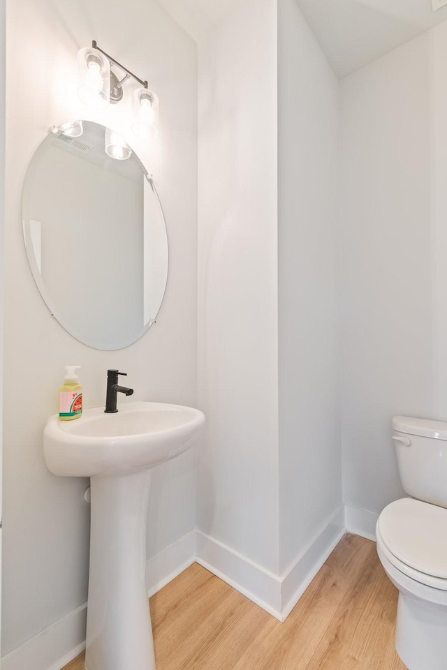 half bathroom with wood finished floors, toilet, and baseboards