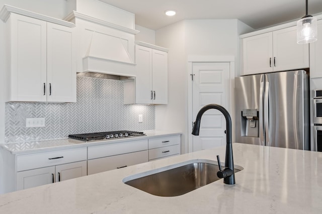 kitchen with appliances with stainless steel finishes, a sink, light stone countertops, and tasteful backsplash