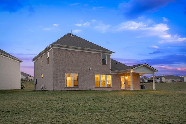 back of house featuring brick siding, a lawn, and central AC unit