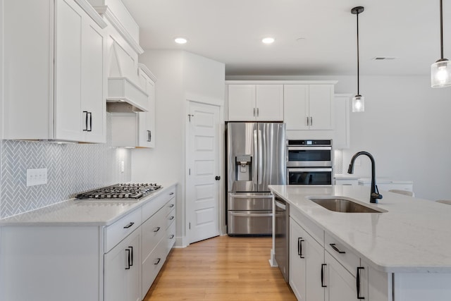 kitchen featuring tasteful backsplash, white cabinets, light wood-style flooring, stainless steel appliances, and a sink