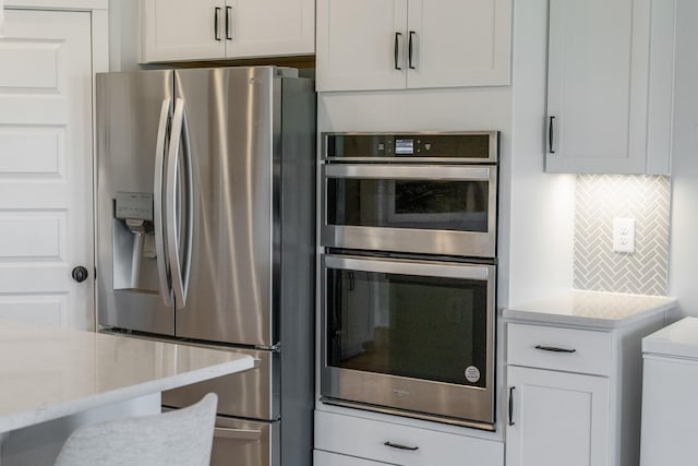 kitchen with white cabinetry, tasteful backsplash, light stone counters, and stainless steel appliances