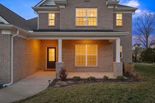 view of front of home featuring covered porch, brick siding, and a front yard