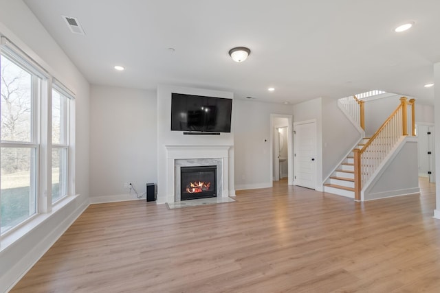 unfurnished living room featuring stairs, a premium fireplace, visible vents, and light wood-style floors