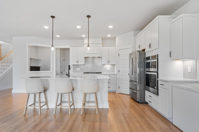 kitchen featuring stainless steel appliances, white cabinets, a sink, light wood-type flooring, and a kitchen bar