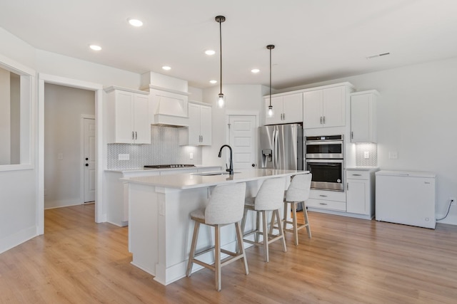 kitchen featuring a breakfast bar area, a kitchen island with sink, stainless steel appliances, light wood-type flooring, and white cabinetry