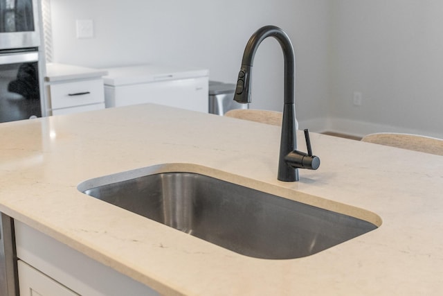 room details featuring light stone counters, stainless steel double oven, white cabinetry, and a sink