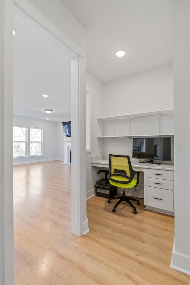 office with light wood-style flooring, a fireplace, baseboards, and built in study area