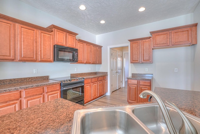 kitchen with light wood-style flooring, brown cabinets, black appliances, a sink, and recessed lighting