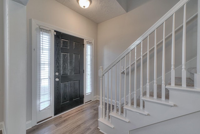 foyer entrance with a textured ceiling, wood finished floors, and stairs