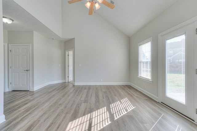 empty room featuring high vaulted ceiling, light wood finished floors, a ceiling fan, and baseboards