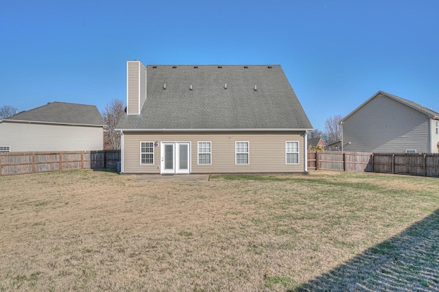 rear view of house with a fenced backyard, a chimney, a shingled roof, and a lawn